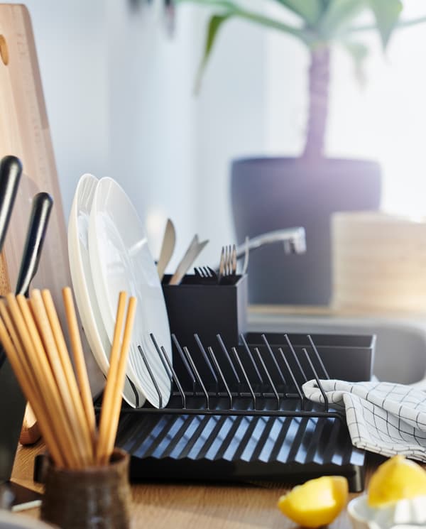 A black dish drainer with a kitchen utensil rack and a plate holder, two white plates, wooden chopsticks and a tea towel.