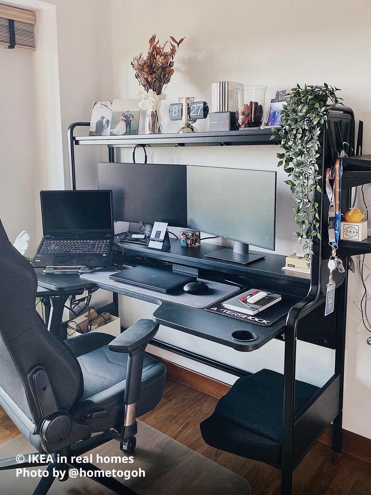 A black FREDDE gaming desk is being used as a home office, featuring two monitors, a laptop stand for a work laptop, a personal laptop, and a notebook placed on the far right of the desk. Photo by instagrammer @hometogoh for IKEA in real homes ©