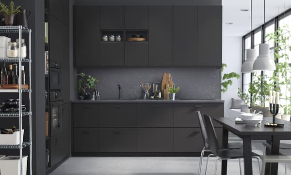 A black kitchen with large windows and a black dining table.