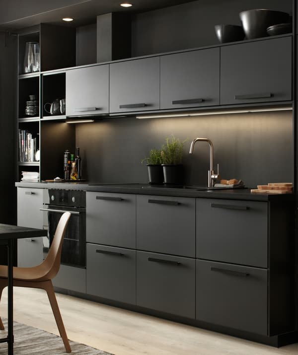 A black kitchen with lighting under the top cupboards.