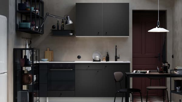 A black KONXHULT kitchen, in a dark modern room, complemented by beige tiles.