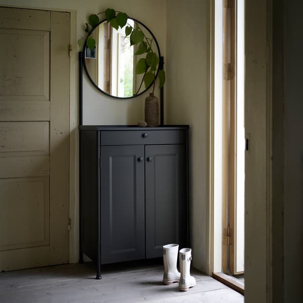 A black KORNSJÖ cabinet with mirror standing in a hallway with gray boots beside it.