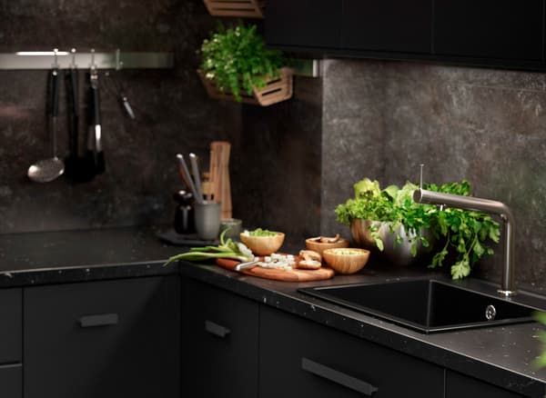 A black KUNGSBACKA kitchen with marble inspired features with kitchen utensils and fresh herbs.