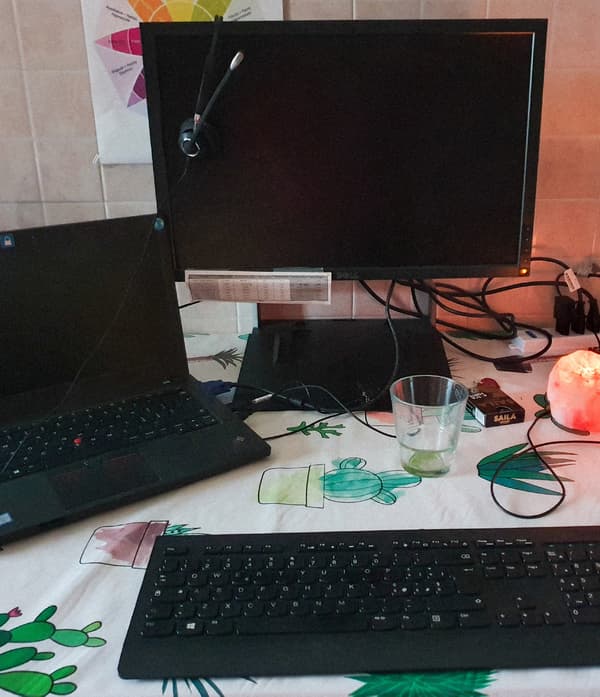A black laptop, a black keyboard and a black computer screen are all standing on a table in a kitchen.