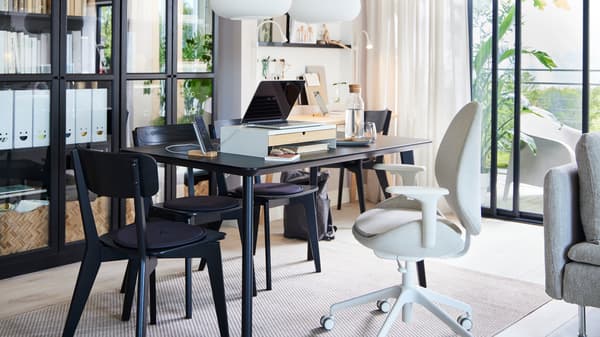 A black LISABO dining table in a bright room in front of glass-door bookcases, set up for work with a laptop.
