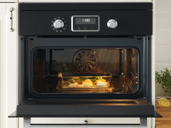 A black microwave combi is open, showing a tray with food and the fan at the back of the oven.