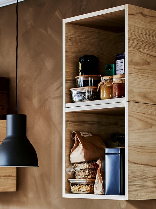 A black pendant lamp hangs next to two, TUTEMO open cabinets mounted vertically on a wall, various food containers inside.