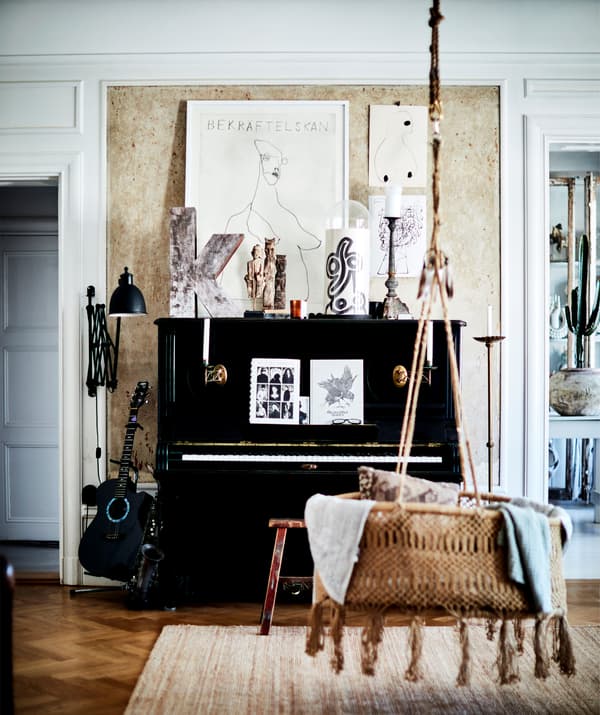 A black piano and a hanging rattan seat in a room with wooden floor.