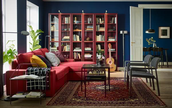A black, red and blue living room with the comfortable KIVIK 3-seat sofa with chaise longue in red placed by the windows.