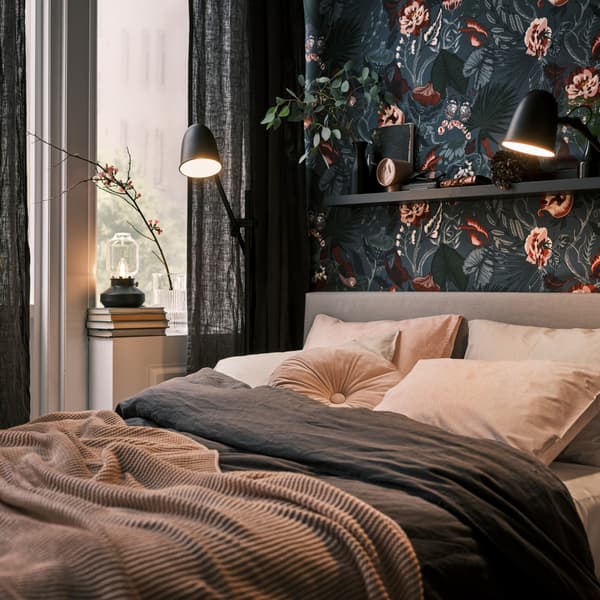 A black SKURUP floor/reading lamp beside a bed, next to a window with dark grey DYTÅG curtains and a TÄRNABY table lamp.