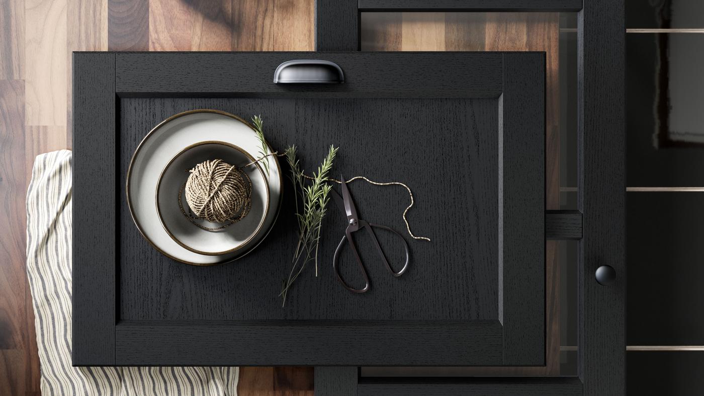 A black stained LERHYTTAN kitchen front on a wooden worktop with accessories on it.