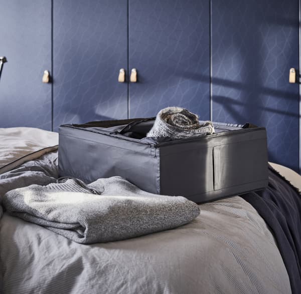 A black storage box on a bed with textiles inside and beside.