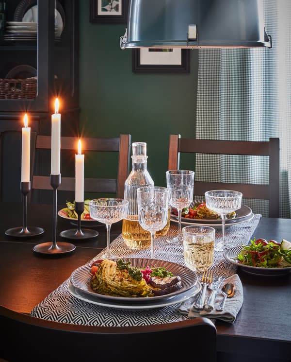 A black table with lit candles, a black/white table-runner, dinner for two and a vintage-looking glassware series.