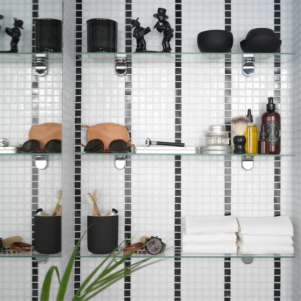 A black/white striped bathroom tile wall where 3 glass shelves are mounted and store towels, decorative items, and more.