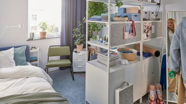 A BLÅKULLEN bed and TROTTEN cabinet combination are in a dorm room. A student holding a skateboard stands by a mirror.
