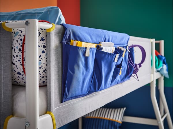 A blue bed pocket that is placed on the guardrail of a white/grey/yellow loft bed.