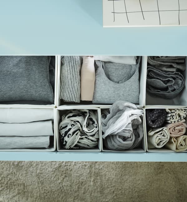 A blue dresser with a drawer open revealing organized clothing in white boxes.
