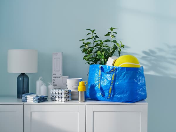 A blue FRAKTA bag on a chest of drawers; the bag is filled with various IKEA purchases. There are other IKEA products on the chest of drawers.