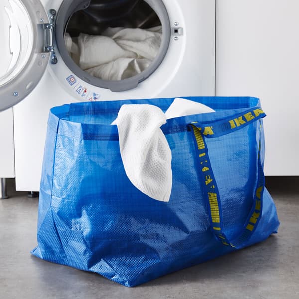 A blue FRAKTA bag sitting on the ground in front of a laundry machine.