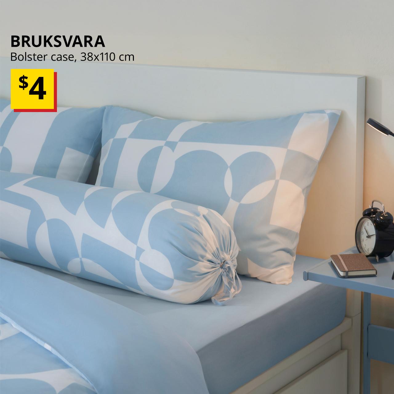 A blue/geometric BRUKSVARA bolster cover.. Black text on top left of the image reads: BRUKSVARA, bolster case, 38x110 cm. Price: $4