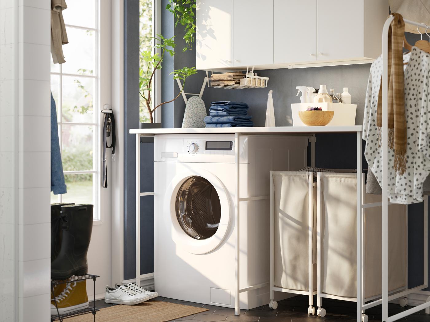 A blue laundry room with a white ENHET storage combination, a washing machine, a clothes rack and laundry baskets on castors.