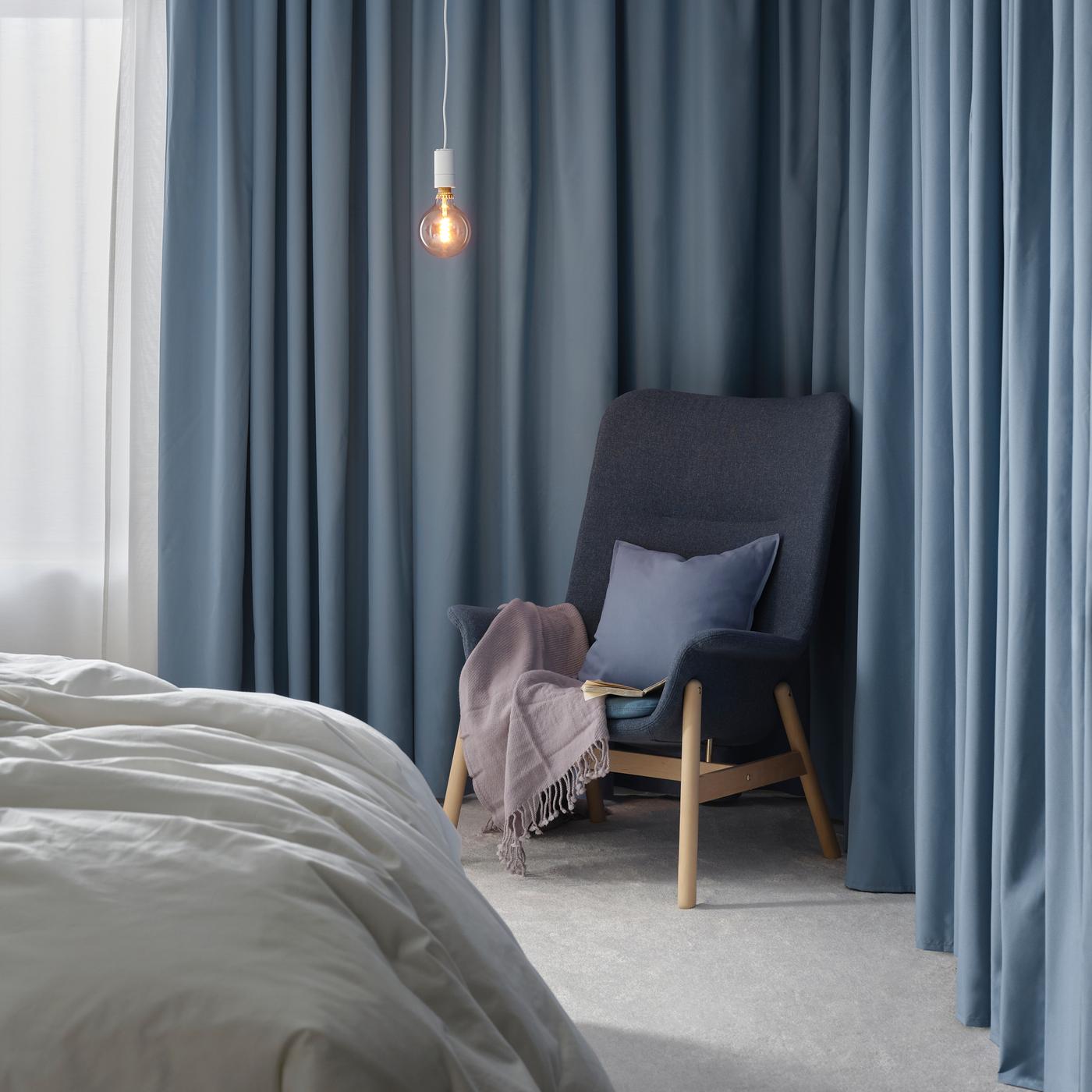 A blue, Scandinavian-styled VEDBO high-back armchair with birch legs holds a throw and cushion in front of blue curtains.