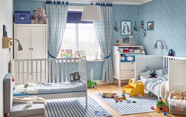 A blue themed baby bedroom with two IKEA SUNDVIK white cots, an IKEA SUNDVIK changing table and a white wardrobe.