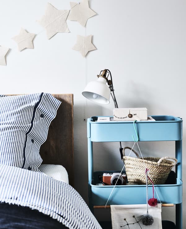 A blue trolley used as a bedside table with lamp.