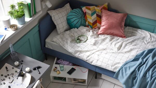 A blue upholstered bed with white/black checked VITKLÖVER bed linen and various cushions, plus FREDVANG under-bed storage.