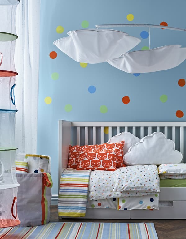 A blue wall with polka dots in a child’s room with a white crib converted into a bed for a toddler.