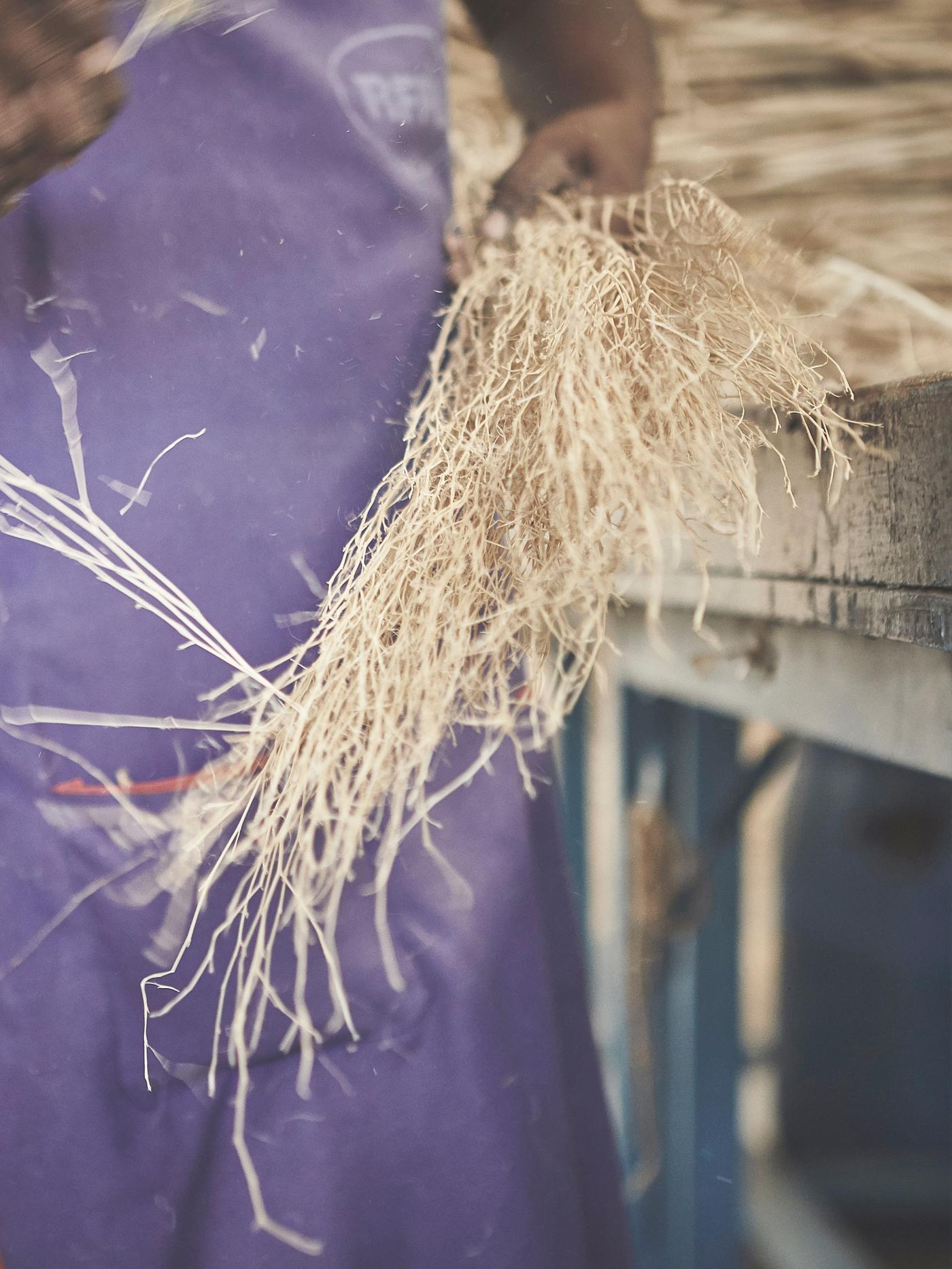 A body of a person in an apron holding a bunch of jute fibres.