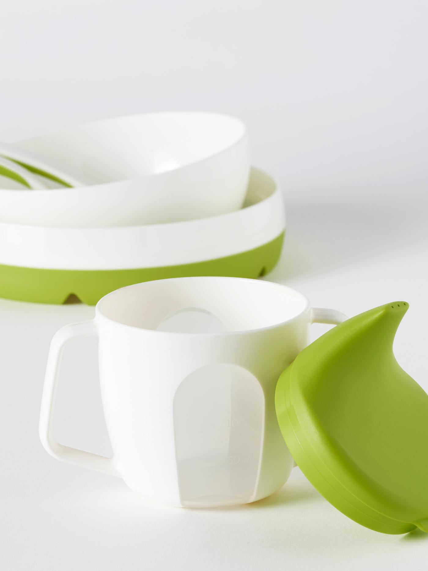 A BÖRJA training beaker stands in front of a SMÅGLI bowl containing two BÖRJA spoons which is on top of a SMÅGLI plate.