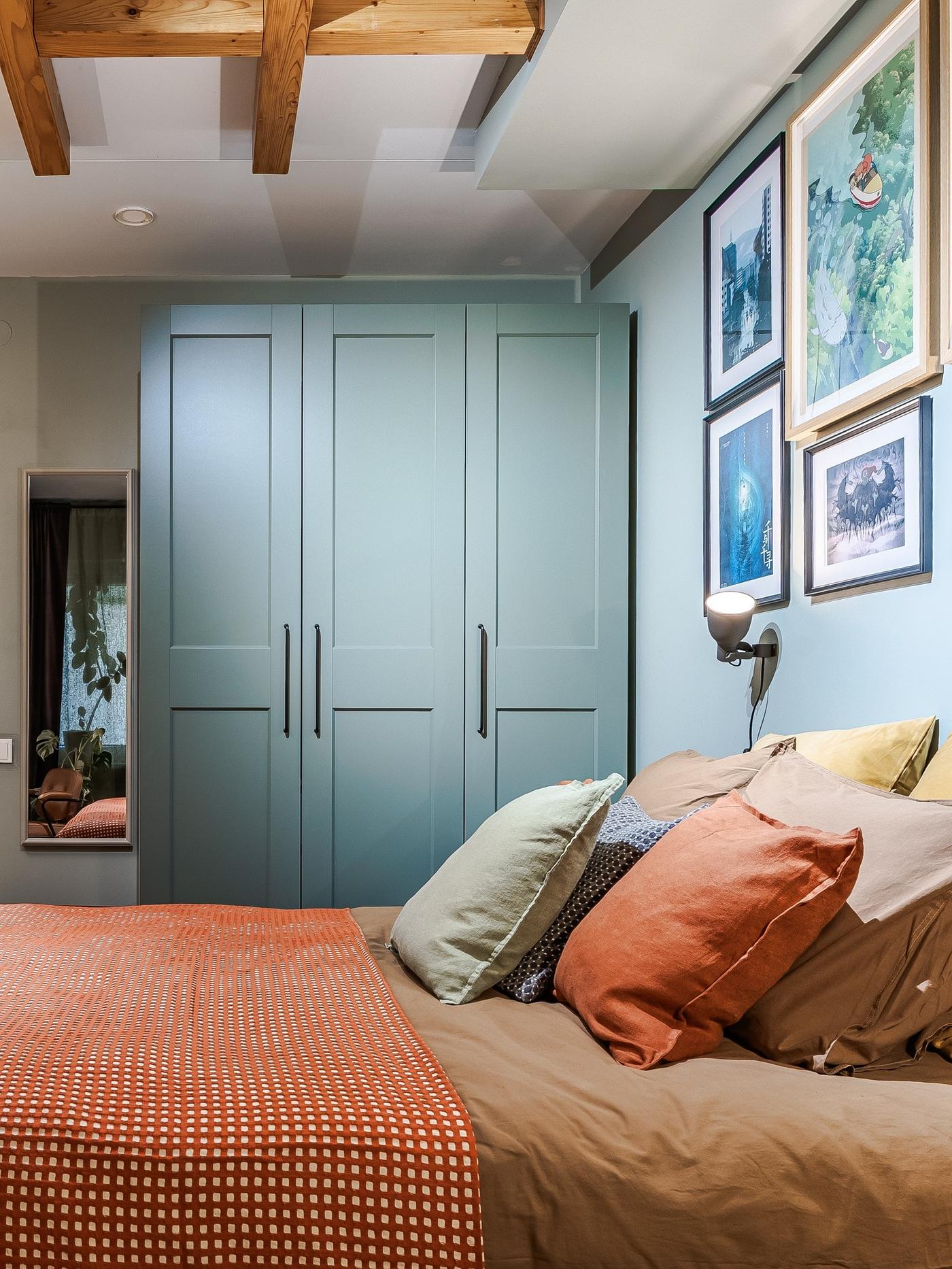 A boho-inspired bedroom featuring an orange bedspread, a blue wardrobe and a collage of posters above the bed.