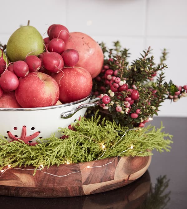 A bowl displays winter fruits, vegetables and greenery.