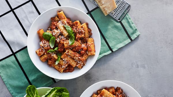 A bowl with pasta Bolognese made from VÄRLDSKLOK plant mince, with fresh basil and grated parmesan, on a kitchen towel.