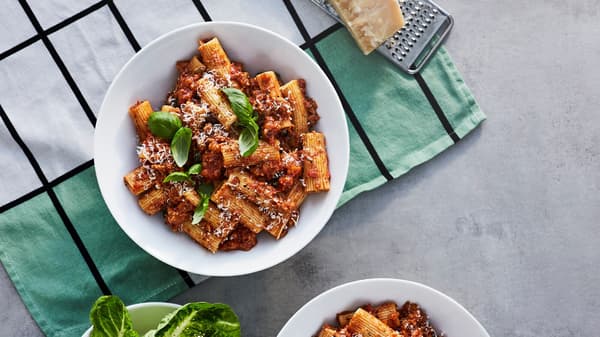 A bowl with pasta Bolognese made from VÄRLDSKLOK plant mince, with fresh basil and grated parmesan, on a kitchen towel.