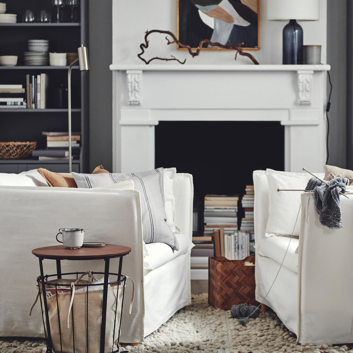 A boxy, white, BACKSÄLEN armchair with a roomy 1,5-seat faces an identical armchair, beside a round storage table.