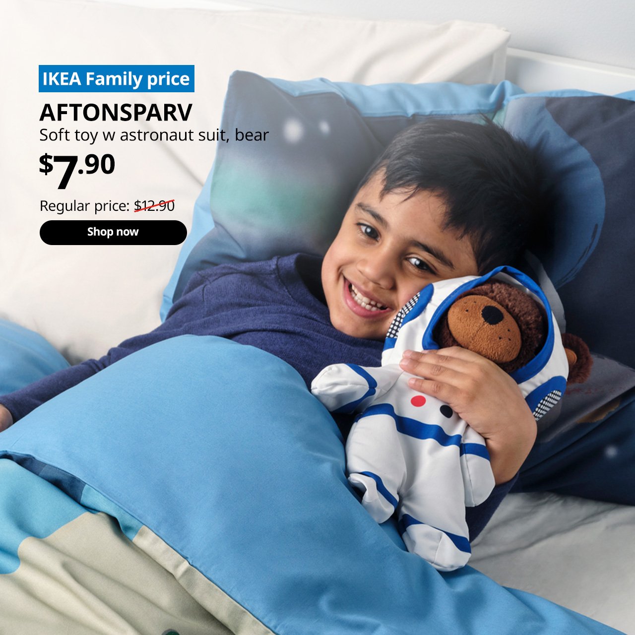 A boy in bed hugging onto a AFTONSPARV bear soft toy in astronaut suit. On the top left corner, a blue tag with white text that reads "IKEA Family price", followed by white text overlaying the image that reads "AFTONSPARV, Soft toy w astronaut suit, bear, $7.90, Regular price $12.90"