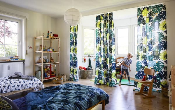 A boy playing in a large bedroom with jungle-themed textiles.