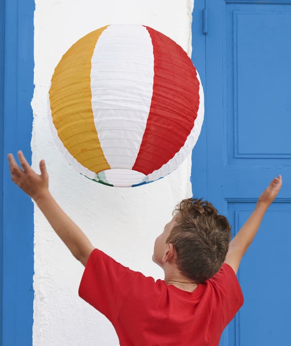 A boy reaching up to a striped hanging lantern.