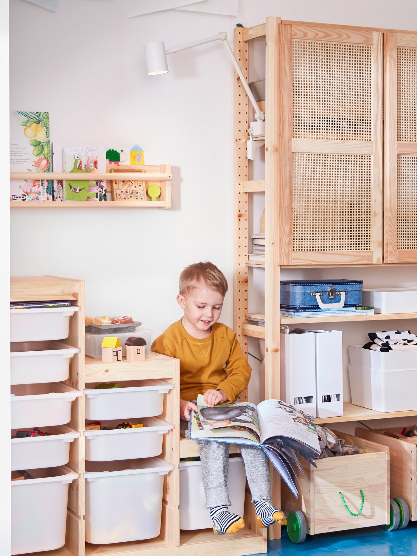 A boy reading a book while sitting on IVAR shelf with a lamp hovering on top.