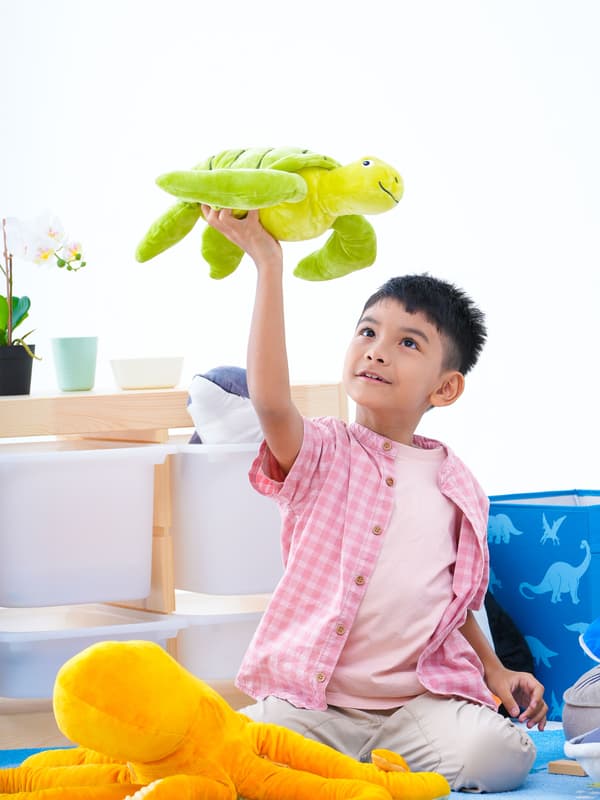 A boy stands on a bed dressed in a BLÅVINGAD whale duvet cover pretending to be a pirate; another boy plays on the floor.