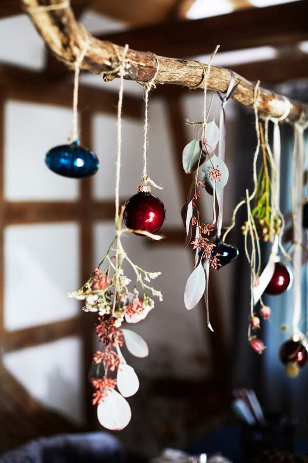 A branch decorated with satin ribbons, Christmas baubles, eucalyptus and dried flowers handing above a dining table.