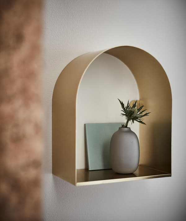 A brass coloured TOSSÅSEN display shelf with a vase and flower.