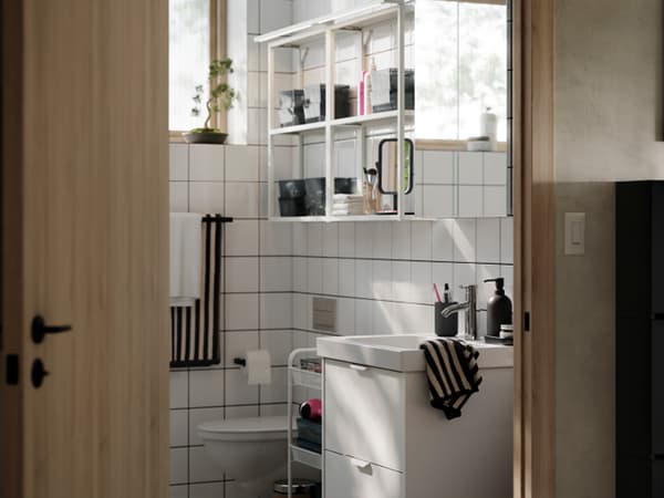 A bright and modern bathroom with white HAVBÄCK/ORRSJÖN storage, ENHET wall shelves with frames and striped towels.