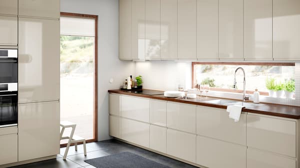 A bright and spacious VOXTORP kitchen in light-beige with glossy doors and fronts, and a BARKBODA worktop in walnut veneer.