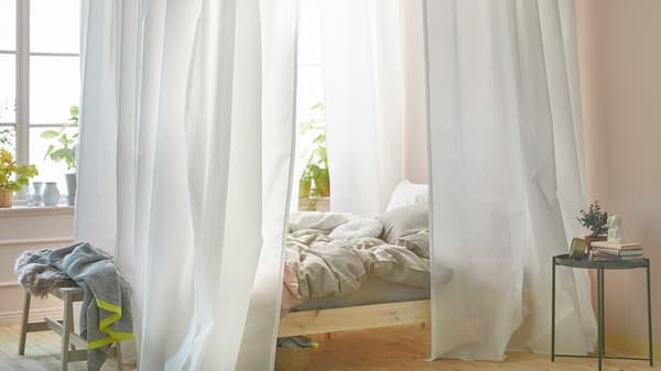 A bright bedroom with a bed near a window. The bed has a canopy made using white curtains and VIDGA curtain tracks.