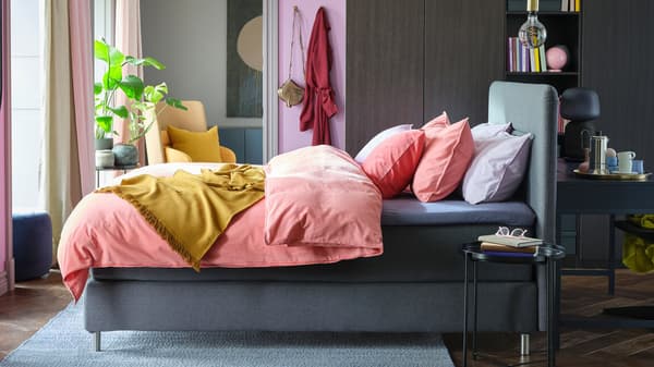 A bright bedroom with a grey FINNSNES divan bed, colourful bedding, and a large PAX/FORSAND wardrobe on one wall.