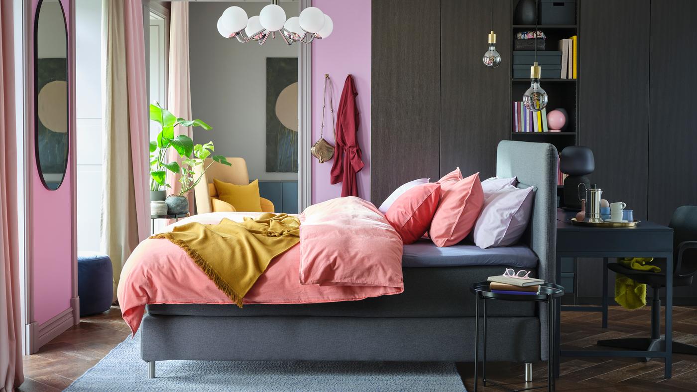 A bright bedroom with a grey FINNSNES divan bed, colourful bedding, and a large PAX/FORSAND wardrobe on one wall.
