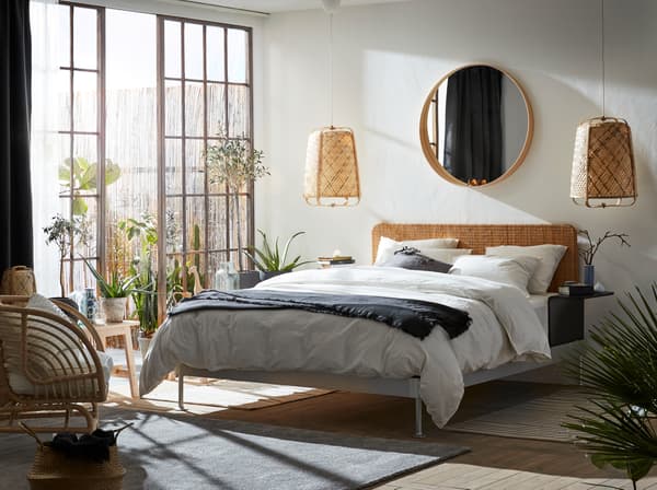 A bright bedroom with a lot of natural materials, like rattan and bamboo. Big glass doors and an outdoor area next to the bed.